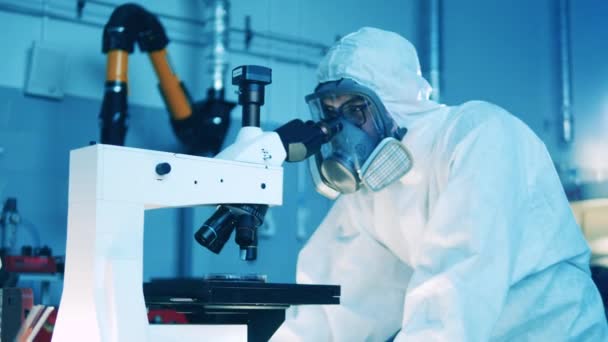 Hombre especialista en un traje de materiales peligrosos está operando un microscopio — Vídeo de stock