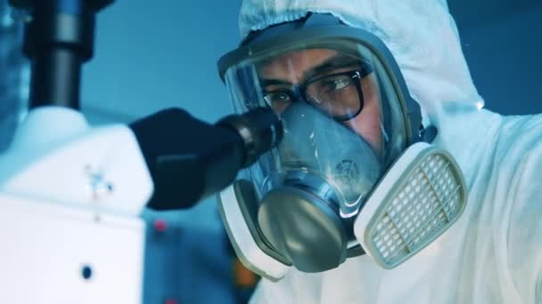 Especialista de laboratorio en un traje de materiales peligrosos está mirando en un microscopio — Vídeos de Stock