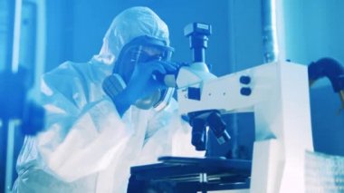 Tehlikeli madde giysisi üzerinde çalışan bir laboratuvar uzmanı mikroskop kullanıyor. Virüs, tıp, bilim konsepti.