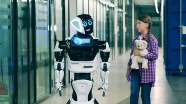 Genç kız bir droidle konuşuyor ve ona oyuncak ayısını gösteriyor.