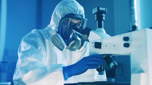 Επιστήμονας με στολή πιτσιλίσματος χρησιμοποιεί μικροσκόπιο. — Αρχείο Βίντεο