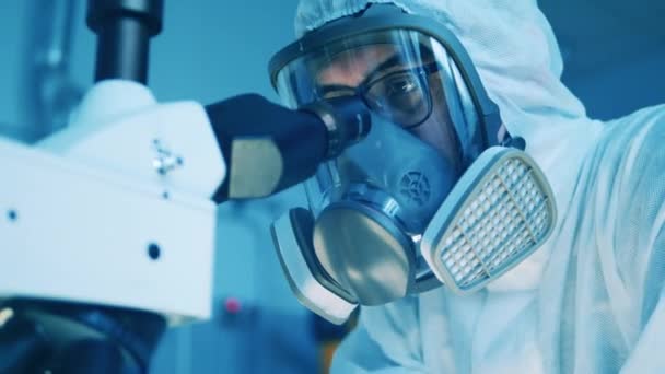 Εργαστηριακός εργάτης με στολή επικίνδυνων υλικών χρησιμοποιεί μικροσκόπιο. — Αρχείο Βίντεο