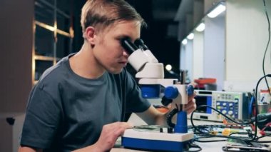 Erkek uzman mikroskop altında devrelere bakıyor.