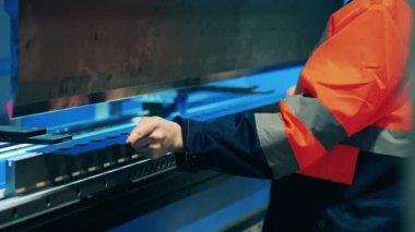Fabrika işçisi elle metal bir plakayı makine kullanarak büküyor.
