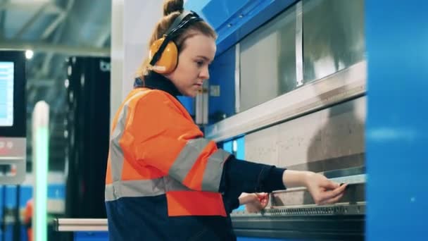 Vrouwelijke werknemer draagt haar hoofdtelefoon tijdens het maken van een metalen onderdeel — Stockvideo