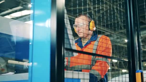男性のエンジニアは、耳のプロテクターを身に着けている間、現代的な機械を動作 — ストック動画