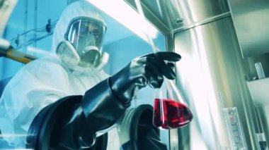 Tehlikeli madde giysisi içindeki laboratuar çalışanı laboratuvar dolabındaki sondaları inceliyor.