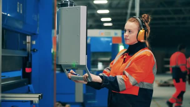 Vrouwelijke werknemer in gehoorbeschermers gebruikt een draagbaar scherm om een machine te bedienen — Stockvideo