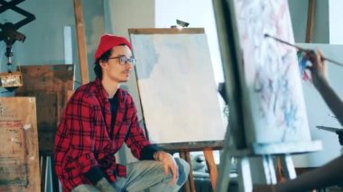 Erkek öğretmen ders sırasında sanat öğrencileriyle konuşuyor.