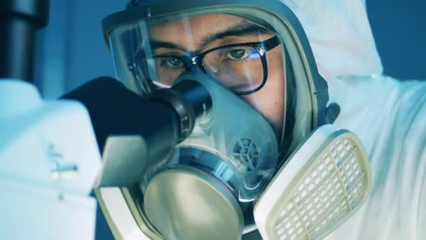 Specialista maschile in una maschera Hazmat sta esaminando microscopio — Video Stock