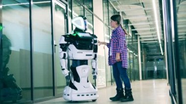 Bir kız onunla sohbet ederken modern bir robota dokunuyor.