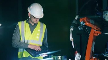 Görevli dizüstü bilgisayar tutarken bir robot cihaz üzerinde çalışıyor.