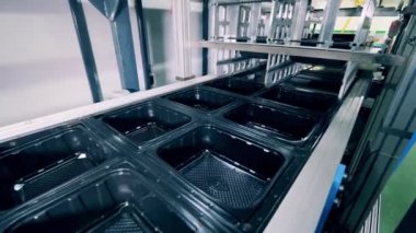 Birçok siyah plastik kap taşıyıcı boyunca hareket ediyor.