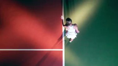 Bir bayan üst manzarada tenis topu servis ediyor.