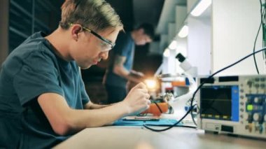 Serviceman in safety glasses fixing smartphone at electronics workshop