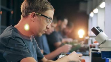 Service people sitting in a row and fixing electronics at workshop