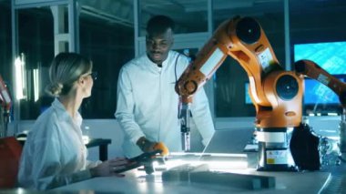 Two science workers are observing industrial robotic arm.