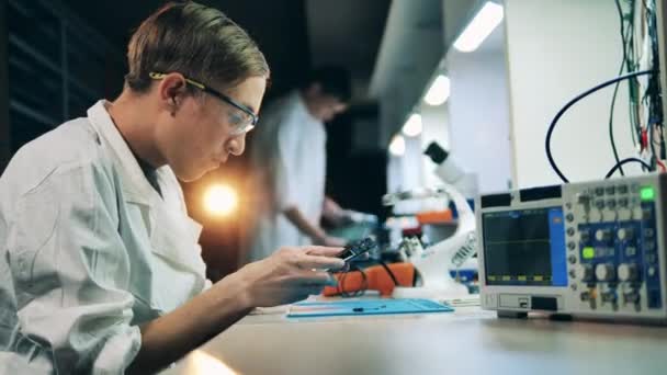 Two workers wearing lab coats fixing electronic devices at workshop — ストック動画