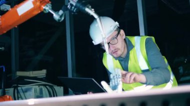 Güvenlik giysisi giyen erkek araştırmacı biyonik bir kolu gözlemliyor.