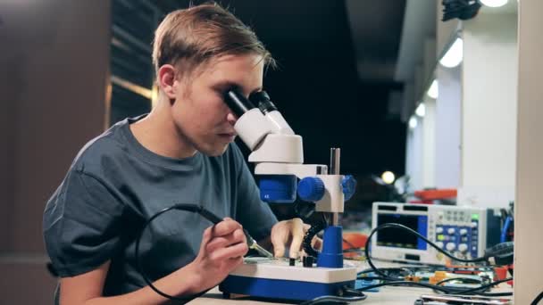 Reparatie specialist op zoek door microscoop op systeembord en solderen — Stockvideo