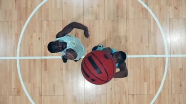 İki Afro-Amerikan oyuncunun basketbol oynadığı bir spor salonunun en üst görüntüsü.