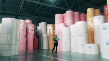 Büyük kağıt rulolarla dolu bir depoyu gözetleyen kadın fabrika işçisi.