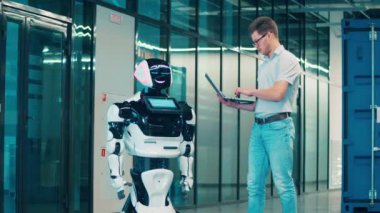 Hizmetli dizüstü bilgisayarla bir androidi kontrol ediyor.