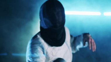 Koruma giysisi giyen bir adam eskrim vuruşları yapıyor.