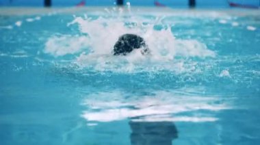 Bir adam havuzda yavaş çekimde kelebek yüzüyor.