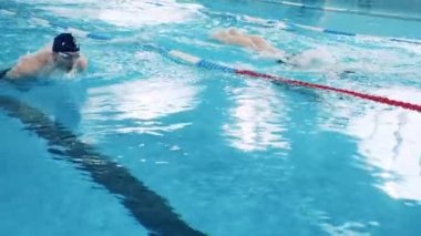 İki adam havuz kenarlarında kelebek yüzüyor.