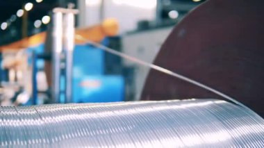 Parlak gümüş tel bir makaradan sökülüyor. Kablo üretimi