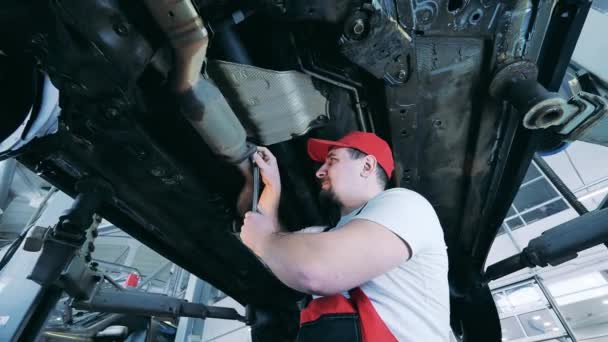 Auto monteur straalt een deel van de auto 's onderkant met een moersleutel — Stockvideo