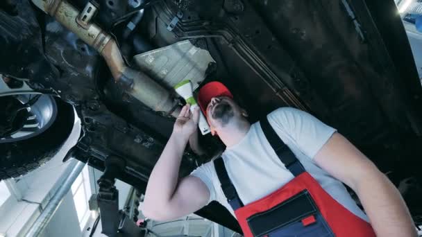 Mechanic inspecteert de onderkant van een auto met een zaklamp. Automobiel mechanisch werk, auto service concept. — Stockvideo