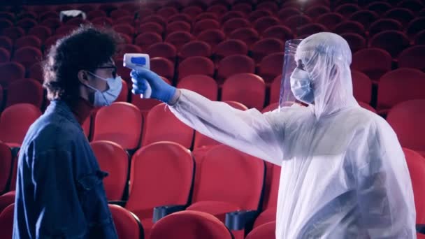 Спеціаліст перевіряє температуру глядачів у кінотеатрі — стокове відео