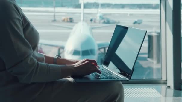 Una mujer está escribiendo en un portátil en la sala de salidas del aeropuerto — Vídeos de Stock