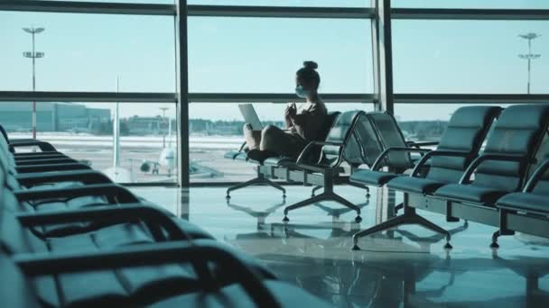 A lady in a face mask is using a laptop in the departure lounge — Stock Video