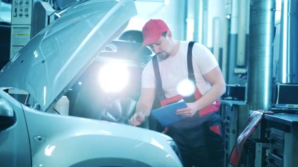 Auto reparateur kijkt onder de motorkap van een voertuig. Auto monteur werkt bij de auto service. — Stockvideo