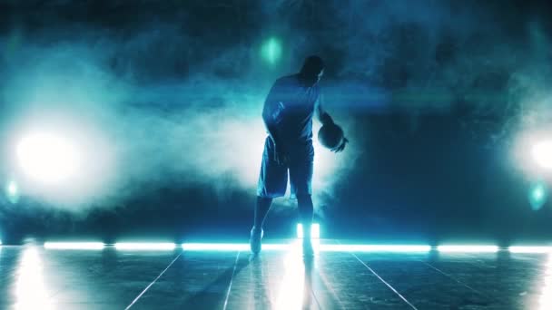 Salón oscuro con un atleta masculino sosteniendo una pelota de baloncesto — Vídeos de Stock
