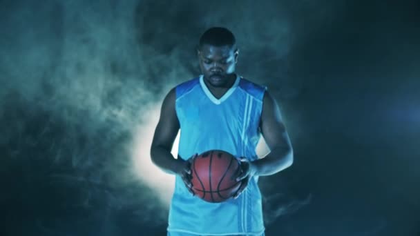 Africký basketbalista drží míč a dívá se do kamery — Stock video