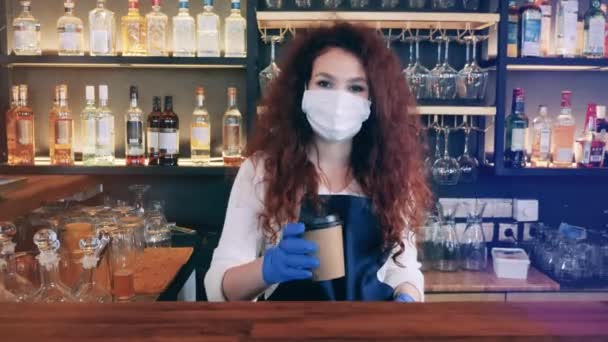 Barista in a face mask gives a cup of coffee to a client — Stock Video