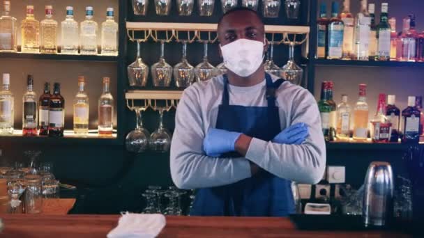 Glimlachende Afrikaanse ober met gezichtsmasker staat achter de bar — Stockvideo