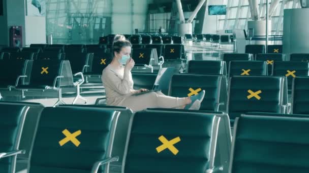 Une dame dans un masque utilise un ordinateur portable parmi les sièges marqués de l'aéroport — Video