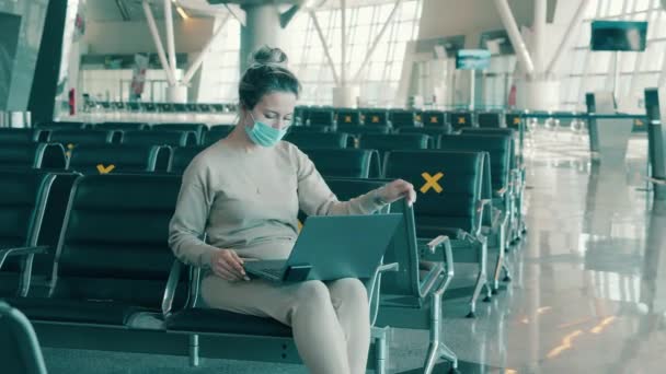 Uma mulher com uma máscara facial está trabalhando em um laptop no aeroporto vazio — Vídeo de Stock