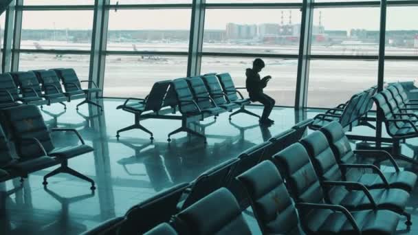 Hall d'aéroport vide avec un garçon sur l'un des sièges marqués — Video