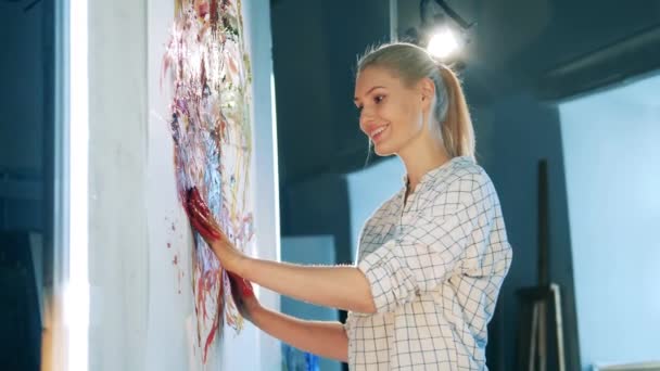 Blond woman is smiling while smearing paint with her hands — Stock Video