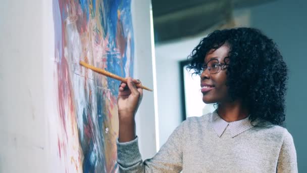 Smiling african ethnicity woman is using a brush to finish a painting — Stock Video