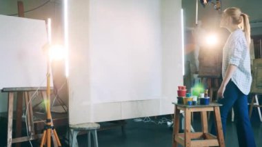 Sarışın bir kadın ve kocaman boş bir tuvalle sanat stüdyosu.