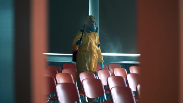 Ein Arbeiter besprüht Stühle in einem Raum, während er desinfiziert. — Stockvideo