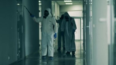 Tehlikeli madde giysileri içindeki işçiler koridoru temizliyor.