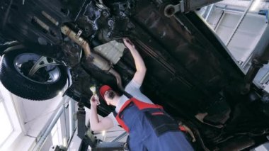 Otomobil tamircisi, el fenerini aşağıdaki aracı incelemek için kullanır.
